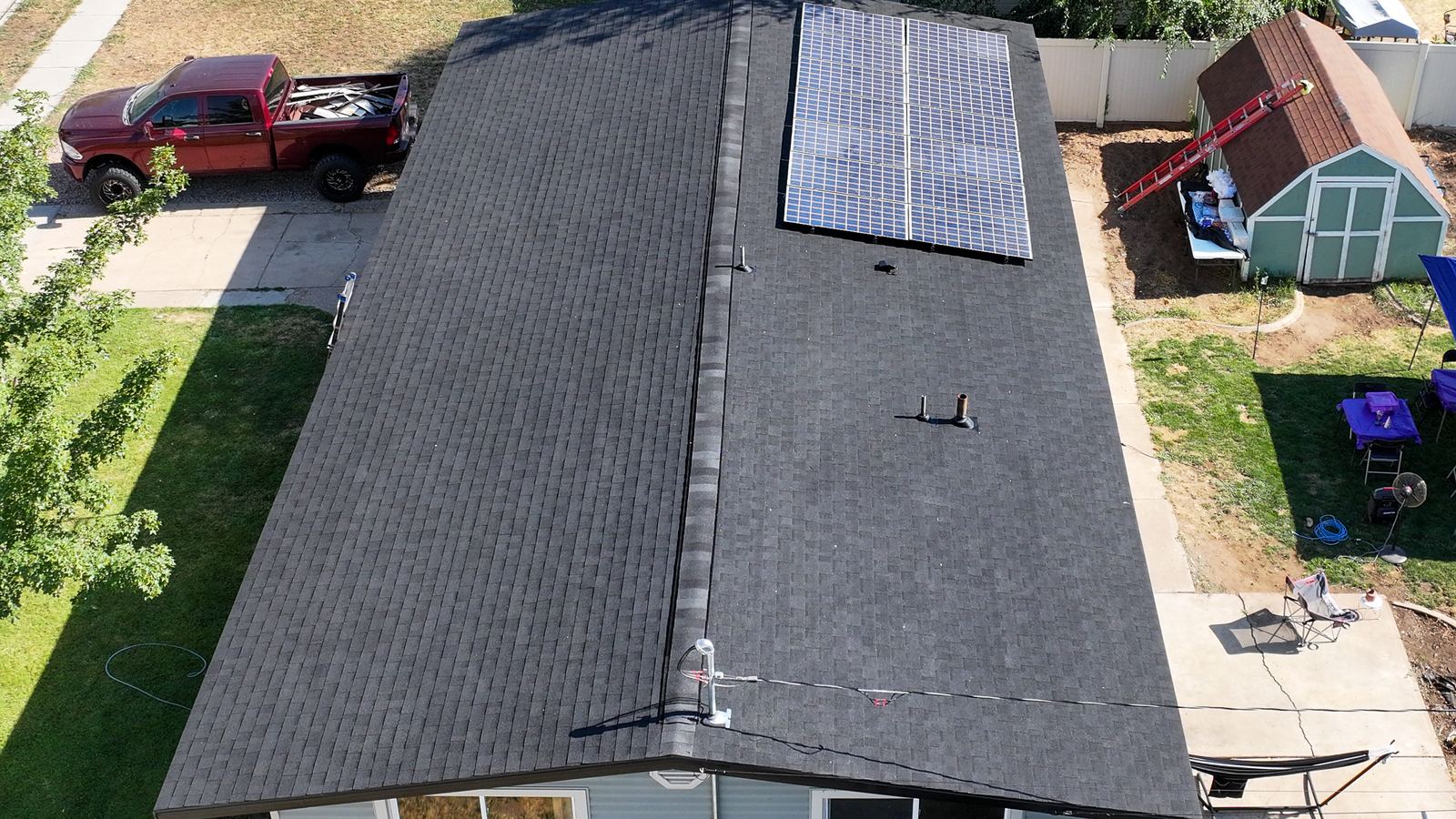 Close aerial view of a dark asphalt shingle roof with a ridge vent, pipe boots and solar panels