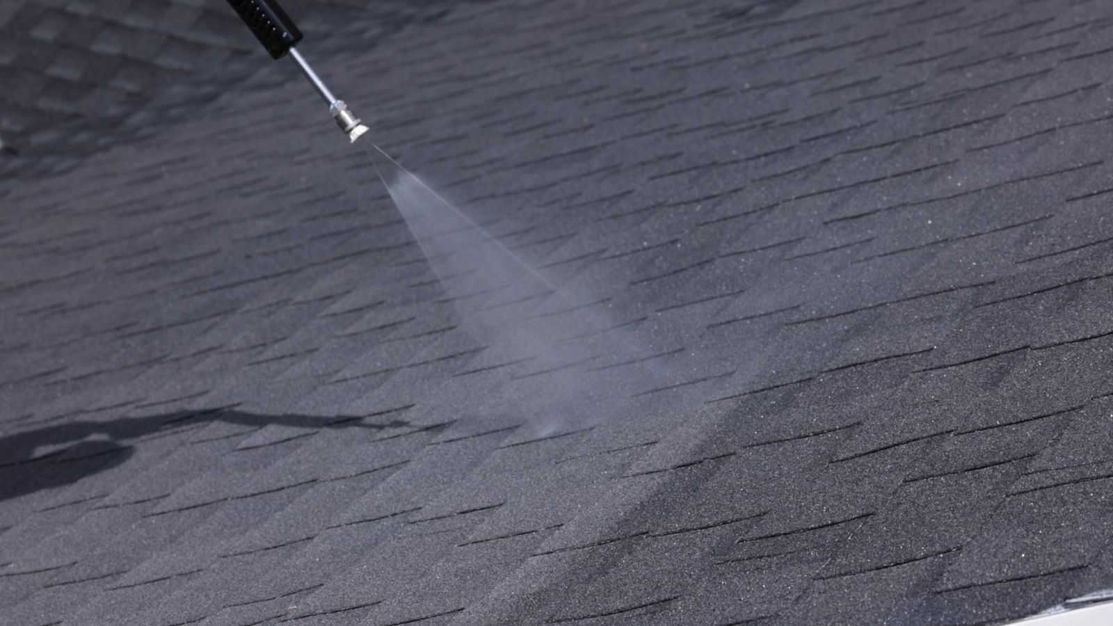 Spray wand applying a roof rejuvenation treatment to dark asphalt shingles