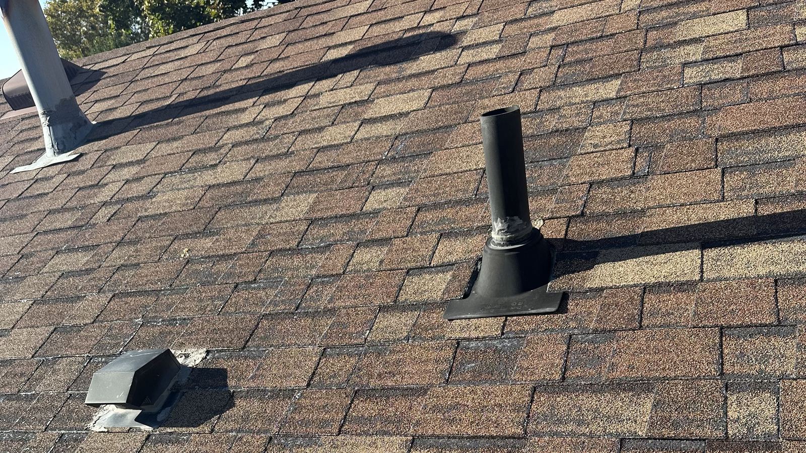 Weathered asphalt shingles with a pipe boot and roof vents, common leak points in heavy rain