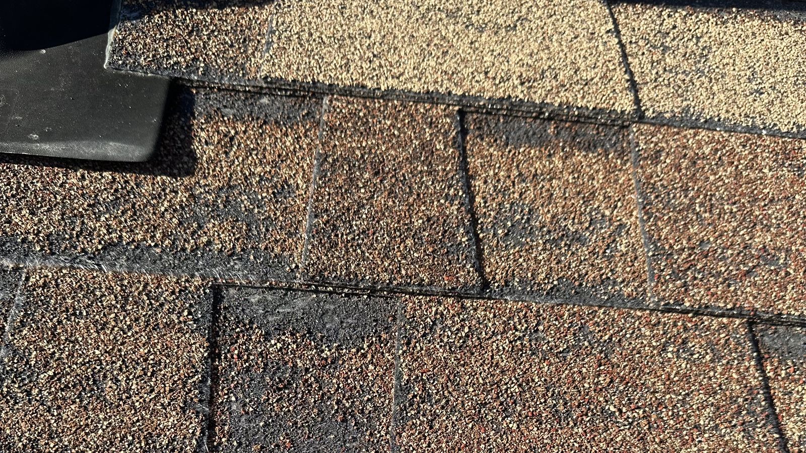 Weathered asphalt shingles showing granule wear near a roof vent