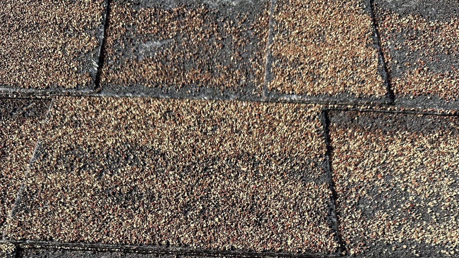 Close-up of Utah asphalt shingles with worn granules and dark exposed patches