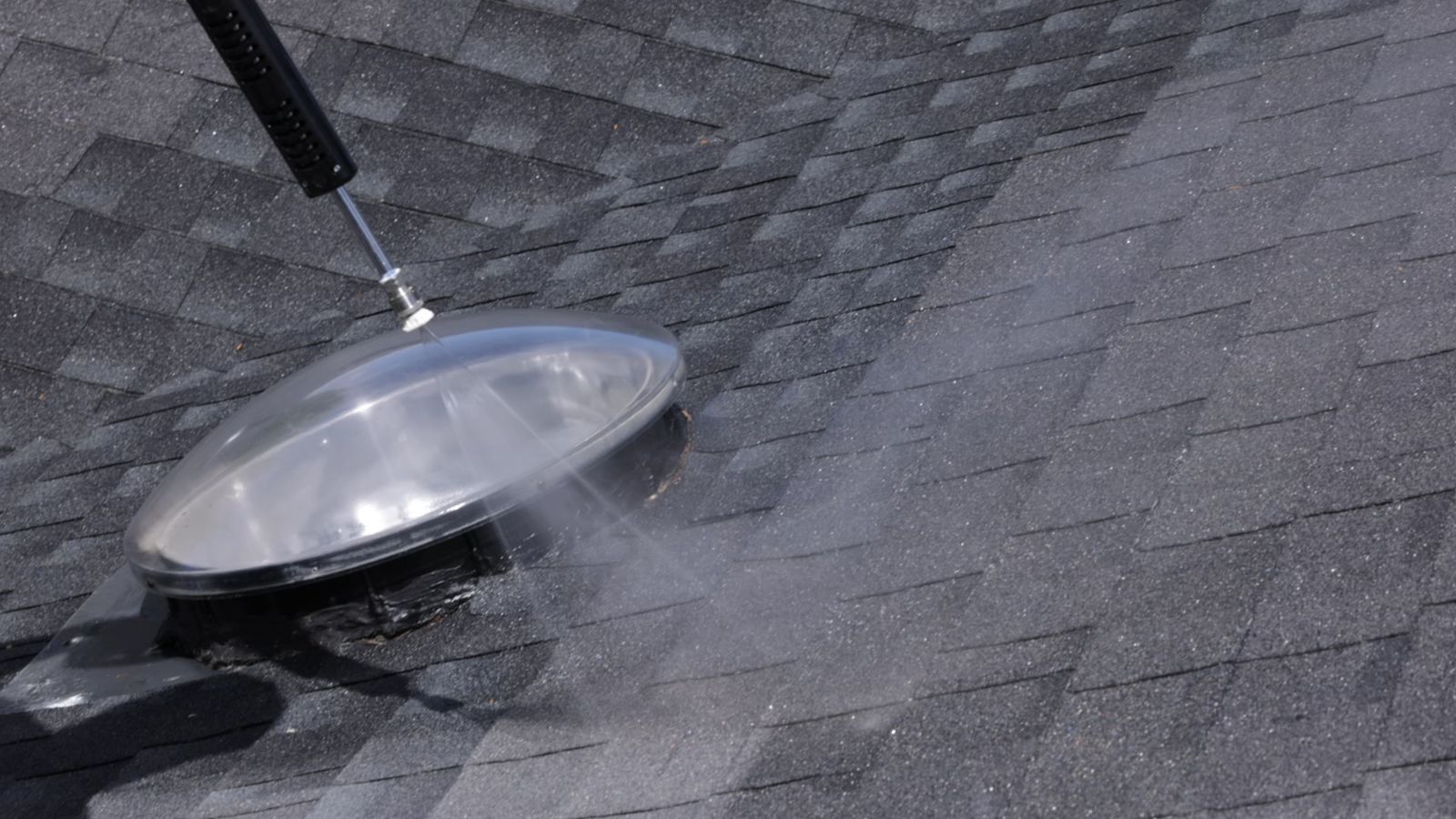 Spray wand applying roof treatment to dark asphalt shingles around a skylight