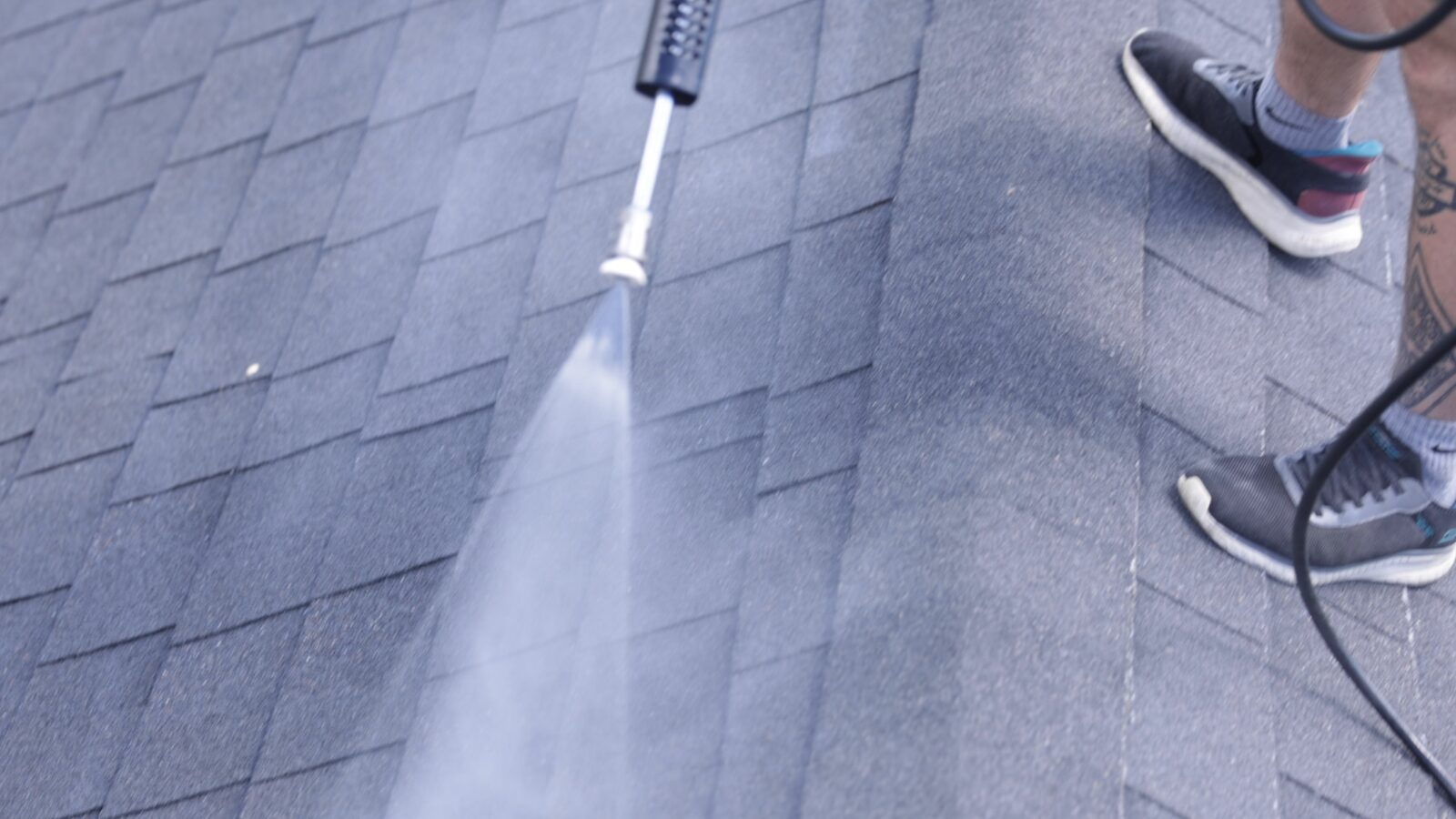 Even GoNano coverage across asphalt shingles from a hose-fed spray wand, with the technician standing on the roof. The NuRoof Guys.