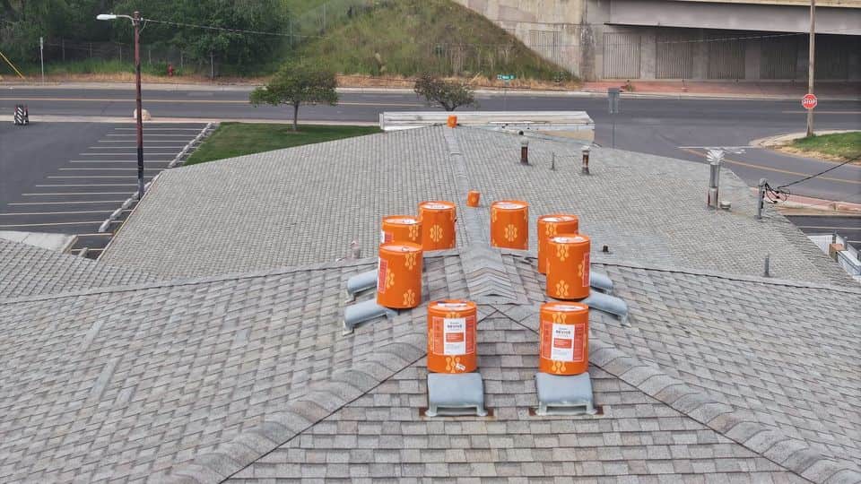 Treatment product buckets staged on a commercial shingle roof. The NuRoof Guys.