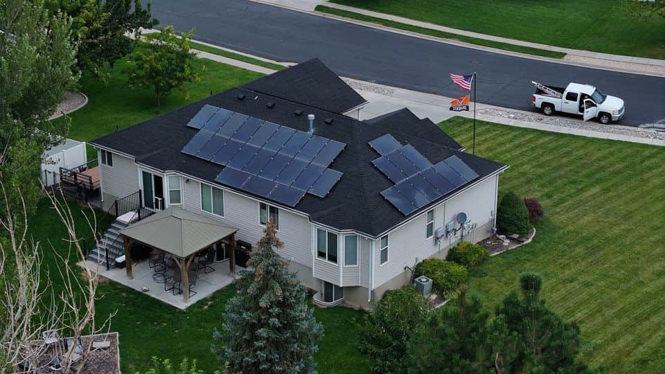 Aerial view of a home with solar panels and a dark shingle roof. The NuRoof Guys.
