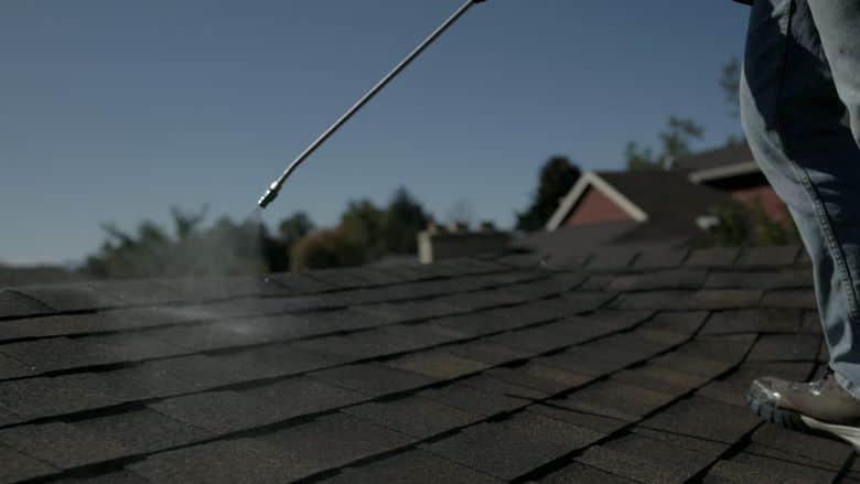 Low-angle view of spray mist on a sunny shingle roof. The NuRoof Guys.
