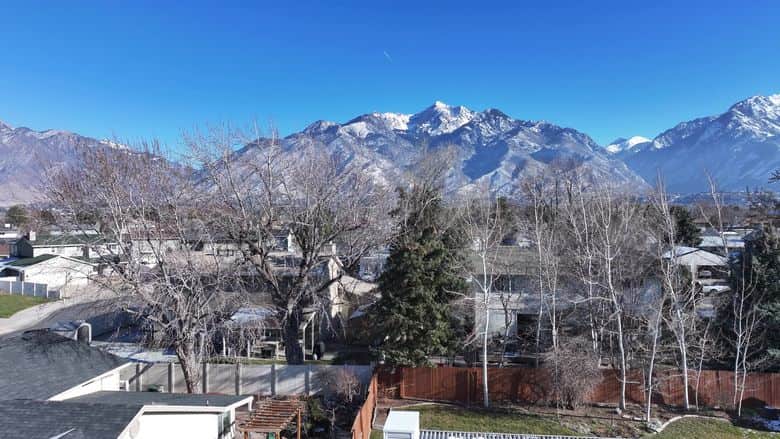 Drone rising over rooftops toward snowcapped Wasatch peaks. The NuRoof Guys.