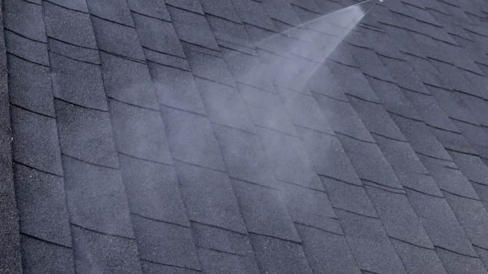 Close-up of a spray fan across dark shingles. The NuRoof Guys.