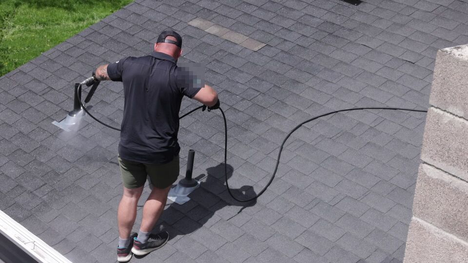 A technician on an asphalt shingle roof applying hose-fed GoNano in Utah.