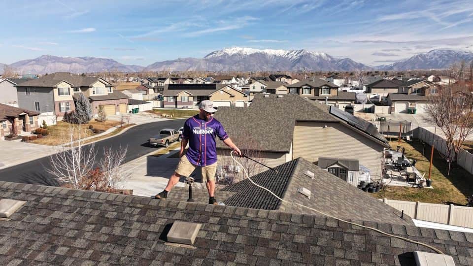 Technician in a NuRoof jersey on a roof overlooking a neighborhood and mountains. The NuRoof Guys.