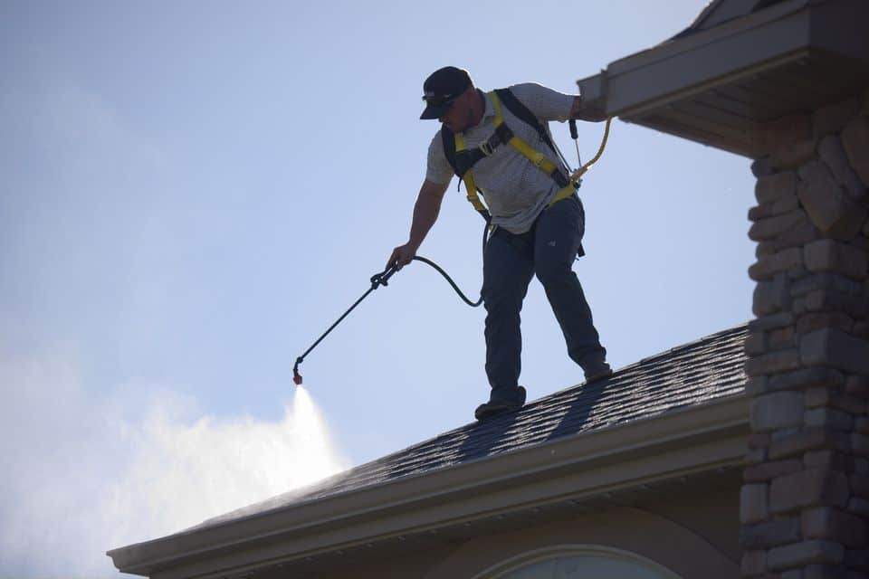 Technician in a safety harness applying GoNano restoration treatment along the edge of an asphalt shingle roof.